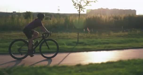 幸せな女性は日没のサイクルパスで自転車に乗っています。魅力的な白人女性は日没時にサイクリングしています。女の子のサイクリストは、公園内の道路自転車にペダルを漕いでいる。サイクリングとトライアスロンのコンセプト。健康的なライフスタイル — ストック動画