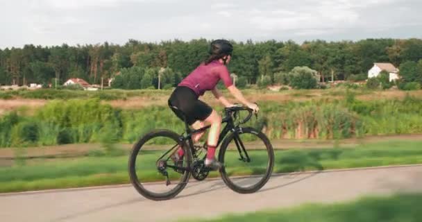 Triatleta donna è in sella a bici da strada sulla pista ciclabile lungo il lungomare. Giovane ragazza sportiva si allena in bicicletta. La ciclista sta pedalando sulla bici da strada. Atleta cavalca in bicicletta all'aperto al tramonto — Video Stock