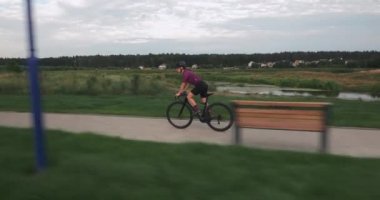 Triatloncu çok hızlı gidiyor. Sıkı çalışma. Bisiklet elbiseli genç bir kadın gezinti güvertesi boyunca bisiklet sürüyor. Bisikletli kız bisikletle pedal çeviriyor. Kadın bisikletçi bisiklet eğitimi alıyor..