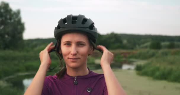 白人のブルネットの女の子は自転車に乗る前に黒いサイクリングヘルメットに置きます。女性サイクリストは、屋外でのサイクリングトレーニングの前にヘルメットをかぶっています。フィットネススポーツ女性で自転車ヘルメットで日没 — ストック動画