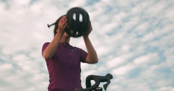 魅力的な幸せな女性は青い空に黒いサイクリングヘルメットを置きます。プロのサイクリストは自転車に乗る準備をしており、安全に乗るためのヘルメットをかぶっています。サイクリングとトライアスロンのコンセプト — ストック動画