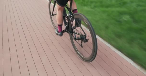 Žena jede na kole do parku. Atletka ve sportovním oblečení jezdí na kole na cyklostezce, stopuje záběr. Cyklistický koncept. Cyklista trénuje kroucení pedálů a jízdu na kole. Cvičení cyklotrasy