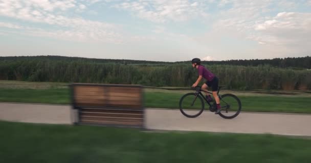 Fit female athlete is pedaling hard out of saddle on road bike. Young woman is cycling fast on bicycle in park. Triathlete rides on bike. Professional sportswoman is training for triathlon competition — Stock Video