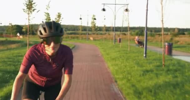 Triathlete woman is cycling fast on road bike at sunset. Pro female cyclist is speeding on aero bicycle in sunshines. Athlete is training hard and preparing for competition. Hard workout on cycle — Stock Video