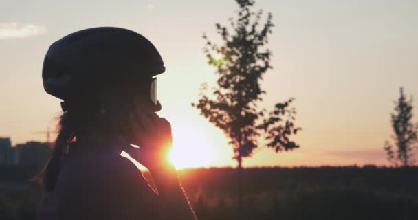 Stylowa piękna rowerzystka rozmawia przez telefon komórkowy na tle miejskich budynków przy złotym zachodzie słońca. Słońce świeci przez dziewczynę mówiącą przez telefon. Koncepcja kolarstwa i triatlonu — Wideo stockowe