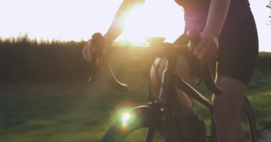 Gün batımında bisiklet süren genç bir kız parkı doldurdu. Bisikletli kadın, gün ışığında bisiklet sürüyor. Güneş ışığı bisikletle parlar. Profesyonel bayan sporcu bisiklet yolunda pedal çeviriyor.