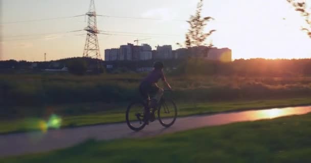 女性サイクリストは日没の公園で自転車を漕いでいます。サイクルパス上の運動選手の女性の乗り物自転車に合う。日没時のサイクリングトレーニング。運動選手は公園のサイクルでペダルをねじる。トライアスロンのコンセプト — ストック動画