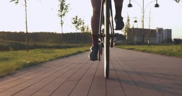 Kvinnan vrider pedaler på väg cykel på cykelvägen vid solnedgången. Kvinnlig cyklist snurrar pedaler på flygcykel. Idrottaren kör för fort på cykel i solnedgångsljus. Cykelväxel och kedja. Cykelhjulsrotation — Stockvideo