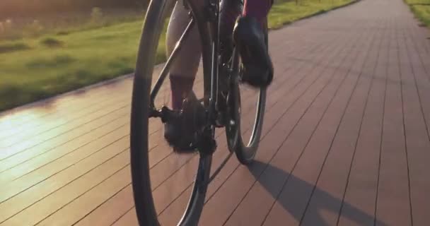 Ruota bici rotazione in luce tramonto. La donna sta pedalando in bici all'alba, da vicino. Ciclista torce pedali in bicicletta sulla pista ciclabile al tramonto. Abbigliamento da ciclismo, catena e cassetta. Concetto sportivo — Video Stock