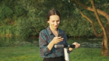 Gömlekli çekici kadın portresi parkta alternatif elektrikli scooter kullanıyor. Ekolojik e-hareketlilik açık havada. Yeni nesil konsepti. Elektrikli scooter kullanan bir iş kadını. Elektrik taşımacılığı