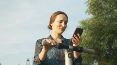 Genç esmer iş kadını alternatif elektrikli taşımacılığa hazırlanıyor. Elektrikli scooter, ekolojik ulaşım. Kız elektrikli scooter 'ın yanında duruyor. Yeni nesil kavramı