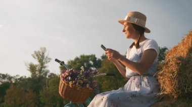 Kadın gün batımında elinde akıllı telefonuyla çayırda dinleniyor. Genç kız parkta dinlenirken cep telefonunu elinde tutuyor. Şapkalı ve şatafatlı bir kadın retro motorla bisiklet sürdükten sonra eğleniyor.