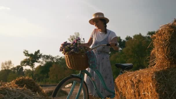 Meadow 'da gün ışığında antika bir motorla duran bir kız. Bisikletli kadın, eski moda bisikleti tarlada yürütür ve yuvarlar. Gün batımında genç ve güzel bir bisikletçinin portresi. İyi tatiller. — Stok video