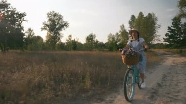 Bisikletli kadın çayırda. Eski model bisikletle gülen mutlu kız tarlada geziyor. Dişi bisikletçi bisiklet sürmekten hoşlanıyor. Güneş ışığında bisikletli güzel bir bayan. Mutlu yaşam tarzı