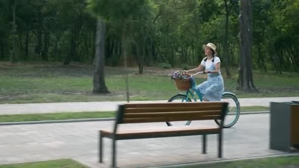 Femme fait du vélo dans le parc au coucher du soleil. Heureuse fille souriante en chapeau et robe fait du vélo sur un vieux vélo vintage à la lumière du coucher du soleil. Femme cycliste insouciante en vélo rétro au coucher du soleil. Mode de vie heureux — Video