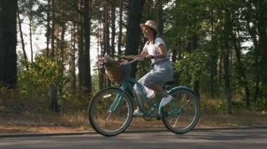 Eski bisikletli genç romantik kız. Kaygısız esmer kadın elbise ve şapka giyerek yaz parkında antika bir bisiklete biniyor. Hippi kız gün batımında şehir parkında bisiklet sürüyor. İyi tatiller.