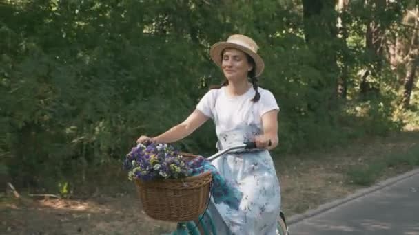 Femme cycliste à vélo. Fille heureuse en robe d'été et chapeau de paille fait du vélo sur vélo rétro par une journée ensoleillée dans le parc. Belle brune chevauchée à vélo. Attrayant jeune femme est à vélo en vacances — Video