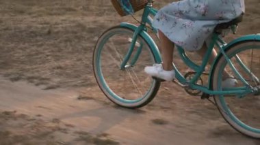 Sahada gün batımında bisiklet tekeri dönüyor. Kadın, gündoğumunda çayırda antika bir bisiklet sürüyor. Elbise giymiş bir kız gün ışığında bisikletle pedal çeviriyor. Mutlu yaşam tarzları. Retro biçimi