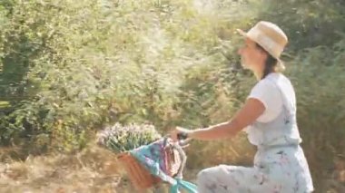 Büyüleyici hayalperest kız yaz parkında klasik bisikletle pedal çeviriyor. Mutlu romantik kadın güneşli bir günde ormanda retro bisiklete biniyor. Şapkalı ve elbiseli genç bayan dışarıda bisikletle eğleniyor ve dinleniyor.