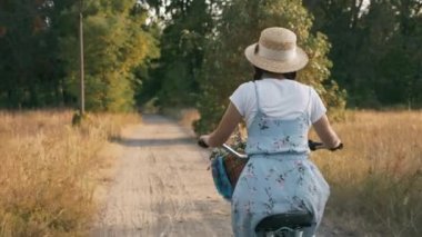 Yazın kırsal kesimde şapkalı ve elbiseli genç bayan eski bir bisiklete biniyor. Kadın bisikletçi gün batımında çayırda bisiklet sürüyor. Esmer kız güneş ışığında orman yolunda klasik bisiklet sürüyor.