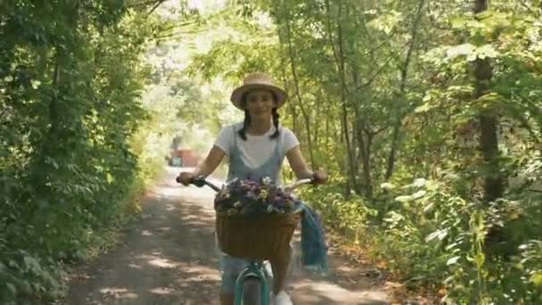 Jeune romantique belle femme en chapeau et robe avec vélo vintage dans la forêt du coucher du soleil. Fille est à vélo avec panier de fleurs. Charmantes promenades à vélo dans le parc en été. Joyeuses vacances — Video