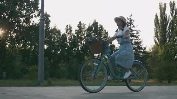 Młoda brunetka jeździ na rowerze po parku miejskim o zachodzie słońca. Ładna urocza dziewczyna jeździ na rowerze retro po parku w świetle słonecznym. Żeński kolarz relaksuje się w parku i dobrze się bawi — Wideo stockowe