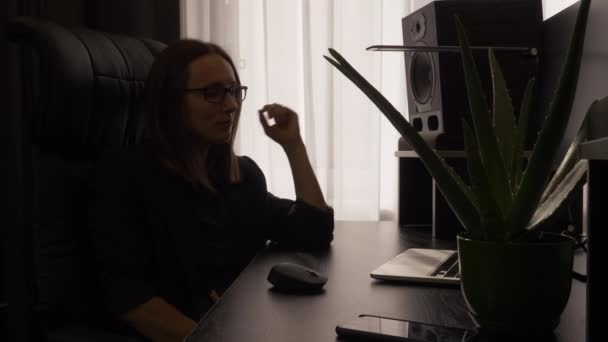 Gözlüklü kadın ofis sandalyesinde sallanıyor ve modern ev işyerindeki bilgisayar ekranına bakıyor. — Stok video