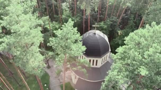 Aerial drone view of Christian church surrounded by green pine trees in forest at sunny day — Stock Video