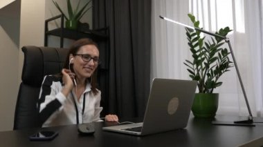 Kulaklık takan kadın iş yerinde görüntülü görüşme yapıyor. İş kadını, ortaklarıyla internet konferansında ofis sohbeti yapıyor. Sanal eğitim konsepti. Evden uzak iş