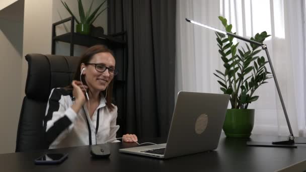 Kvinnan i hörlurar ringer videokonferens på hemmakontoret. Affärskvinna gör online konferens distans office chat med partners. Virtuell träning koncept. Fjärrarbete hemifrån — Stockvideo