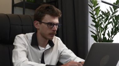 Genç işadamı modern ofis masasında oturuyor, dizüstü bilgisayarı kapatıyor ve işini bitiriyor. Gözlüklü beyaz sakallı adam iş yerinde dizüstü bilgisayarla çalışıyor.