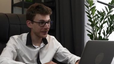 Genç işadamı görüntülü görüşme ile konuşuyor. Adam uzak işyerindeki web kamerasıyla iş arkadaşlarıyla internet üzerinden toplantı yapıyor. Erkek ofiste çalışıyor.