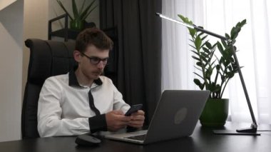 Kendine güvenen genç iş adamı modern ofis masasında otururken akıllı telefon kullanıyor. Elinde cep telefonu olan beyaz erkek işçi ofiste çalışıyor.