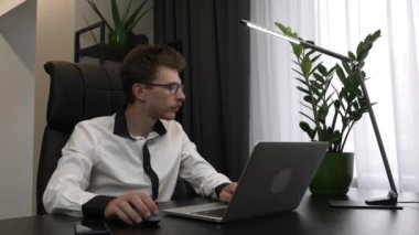 Gözlüklü genç işadamı işe ara veriyor. Çok çalışan yorgun adam, ofiste çalışmayı ve dizüstü bilgisayarı kapatmayı bitiriyor. Erkek işçi modern ofis işyerindeki bilgisayarda çalışıyor