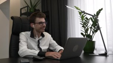 Kulaklıklı heyecanlı genç iş adamı modern ofis masasında oturmuş müzik dinliyor. Gözlüklü beyaz yakışıklı adam iş yerinde kulaklıklardan müzik dinliyor.