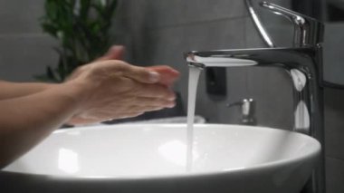 Kadın ellerini sabun ve sıcak suyla yıkıyor, parmaklarını sıkça ovuyor. Coronavirus salgını önleme. Kadın ellerini lavaboda köpükle yıkar.