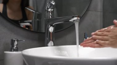 Beyaz kadın lavaboda sabunla ellerini yıkıyor. Modern banyodaki kadınlar ellerini köpükle yıkarlar, parmaklarını ovuştururlar, su ellerden akar, koronavirüs salgınını önlemek için.