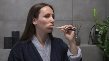 Genç beyaz kadın modern banyoda dişlerini fırçalıyor. Güzel esmer kadın diş fırçası ve diş macunuyla dişlerini fırçalıyor. Ağız temizliğine karşı ağız temizliği yapıyor.