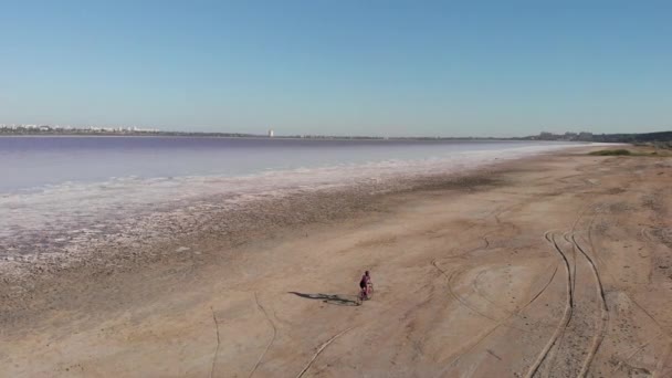 Женщина-путешественница едет на велосипеде по высохшему соленому озеру. Женщина ездит на велосипеде вдоль берега Куяльника, Украина — стоковое видео