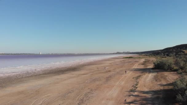 Luchtfoto van wateroppervlak en gedroogde kust op Kuyalnik, Odessa, Oekraïne. Drone vliegt over het zoute zand van de kustzone op Kuyalnik Liman met vrouwenritten op de fiets langs de kustlijn — Stockvideo