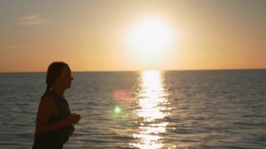 Yoğunlaşmış esmer kadın gün doğumunda koşuyor ve deniz kıyısında sabah egzersizleri yapıyor. Güzel bayan atlet gün batımında sahil boyunca koşar. Sağlıklı yaşam tarzı kavramı