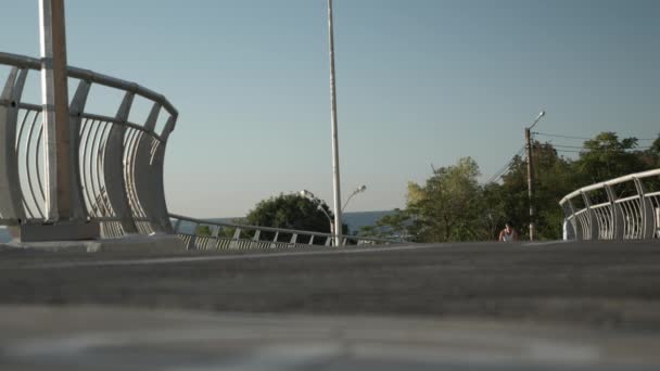 Giovane donna caucasica elegante va in bicicletta sul ponte all'alba. Felice, emotivo sorridente giovane donna millenaria è in sella alla bicicletta attraverso il lungomare in bella luce del tramonto, guardando il tramonto — Video Stock