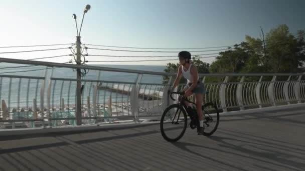 Sportowe fitness dziewczyna w stylowym stroju casual jest jazda na rowerze powietrznym drogi wzdłuż promenady plaży w słoneczny letni dzień. Szczęśliwa kobieta z pięknym muskularnym ciałem jeździ na rowerze o wschodzie słońca — Wideo stockowe
