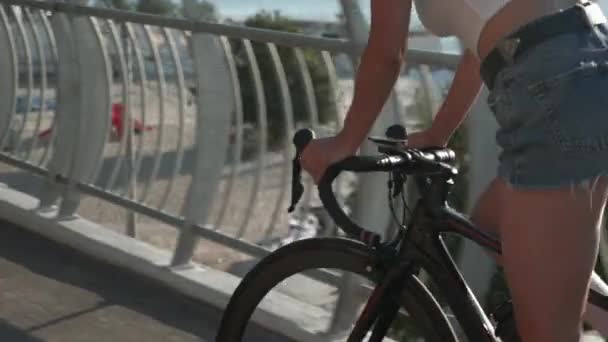 Mooie vrouw fietser fietst langs strand promenade in de ochtend met de zee op de achtergrond. Vrouwelijke fietser in stijlvolle casual kleding is fietsen op de fiets op de brug in zonlicht bij zonsopgang — Stockvideo