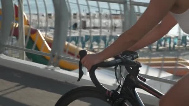 Close-up van vrouwelijke fietser handen op stuur van racefiets. Vrouw fietst langs strandpromenade in zonlicht. Meisjes fietsen 's morgens bij zonsopgang op een lege brug. Fietsconcept — Stockvideo