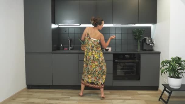 Divertida mujer morena activa está bailando en la cocina moderna por la mañana. Mujer bastante joven está utilizando el teléfono inteligente y divertirse en casa. Baile enérgico de la feliz dama sonriente — Vídeos de Stock
