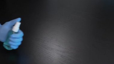 Mavi tıbbi eldiven siyah arka planda el dezenfektanı spreyi tutuyor. Coronavirus salgını ve grip virüsünün önlenmesi. Tıp konsepti