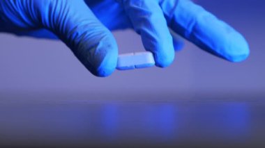 El, beyaz hapı siyah arka plana koyuyor. Doktor ağrı kesici hapı tutuyor, yakın çekim. Eczane ve tedavi konsepti. Coronavirus, covid-10 virüsü ve grip enfeksiyonunu önleme
