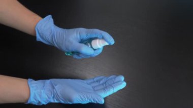 Kadın, el dezenfektanı spreyiyle mavi tek kullanımlık eldivenlerle ellerini ovuşturuyor. Kadın doktor veya hemşire, covid-19 salgınını önlemek için elleri alkol dezenfekte edici ile dezenfekte ediyor.