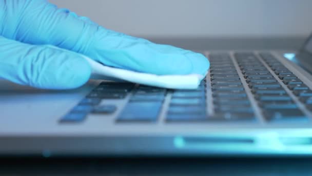 Vrouwelijke hand wrijft laptop computer met ontsmettingsmiddel en natte veeg in het kantoor tijdens quarantaine. Hygiëne van de werkplek om virusinfectie te voorkomen, close-up van de hand in medische blauwe handschoen — Stockvideo